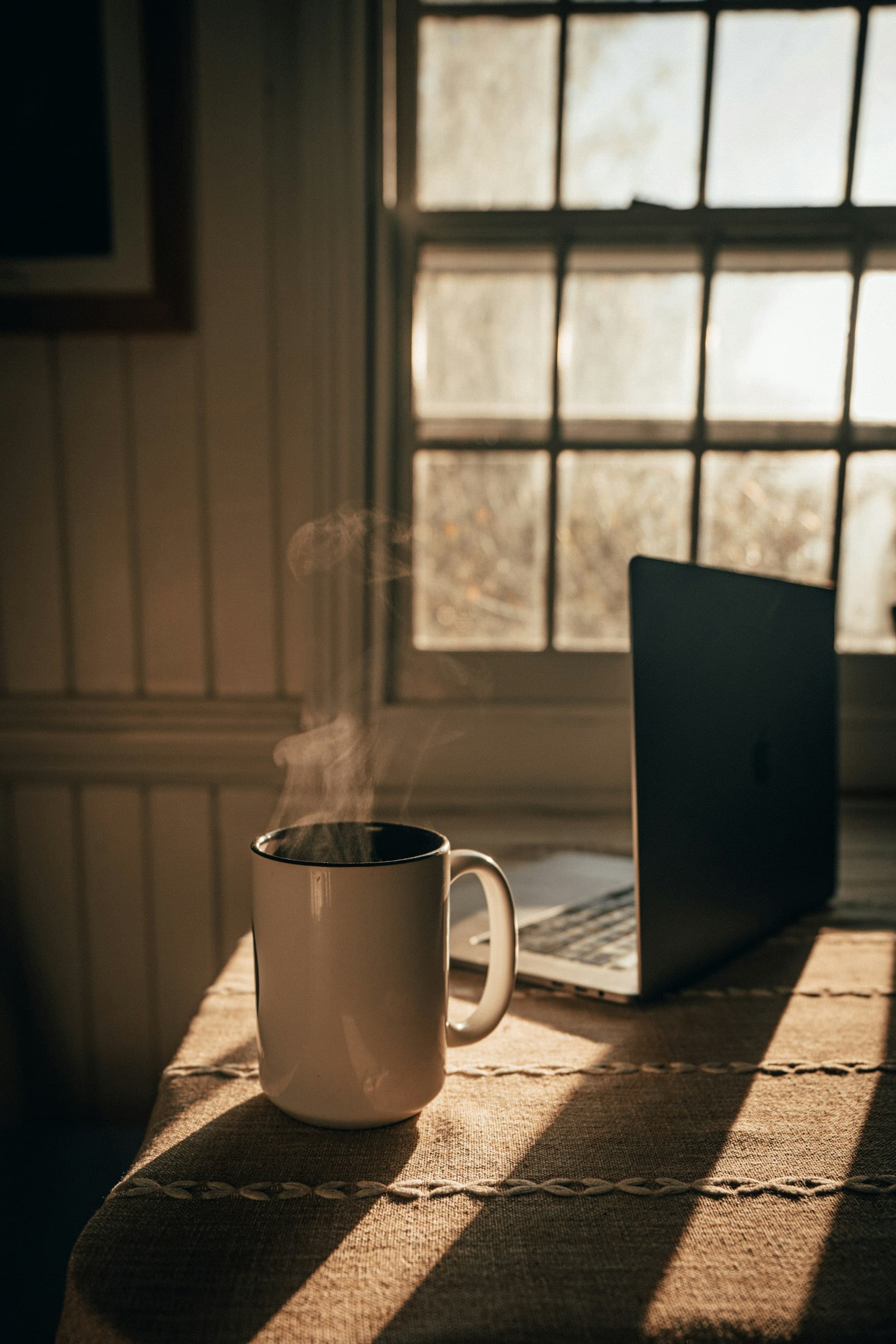 A laptop and a coffee in window light