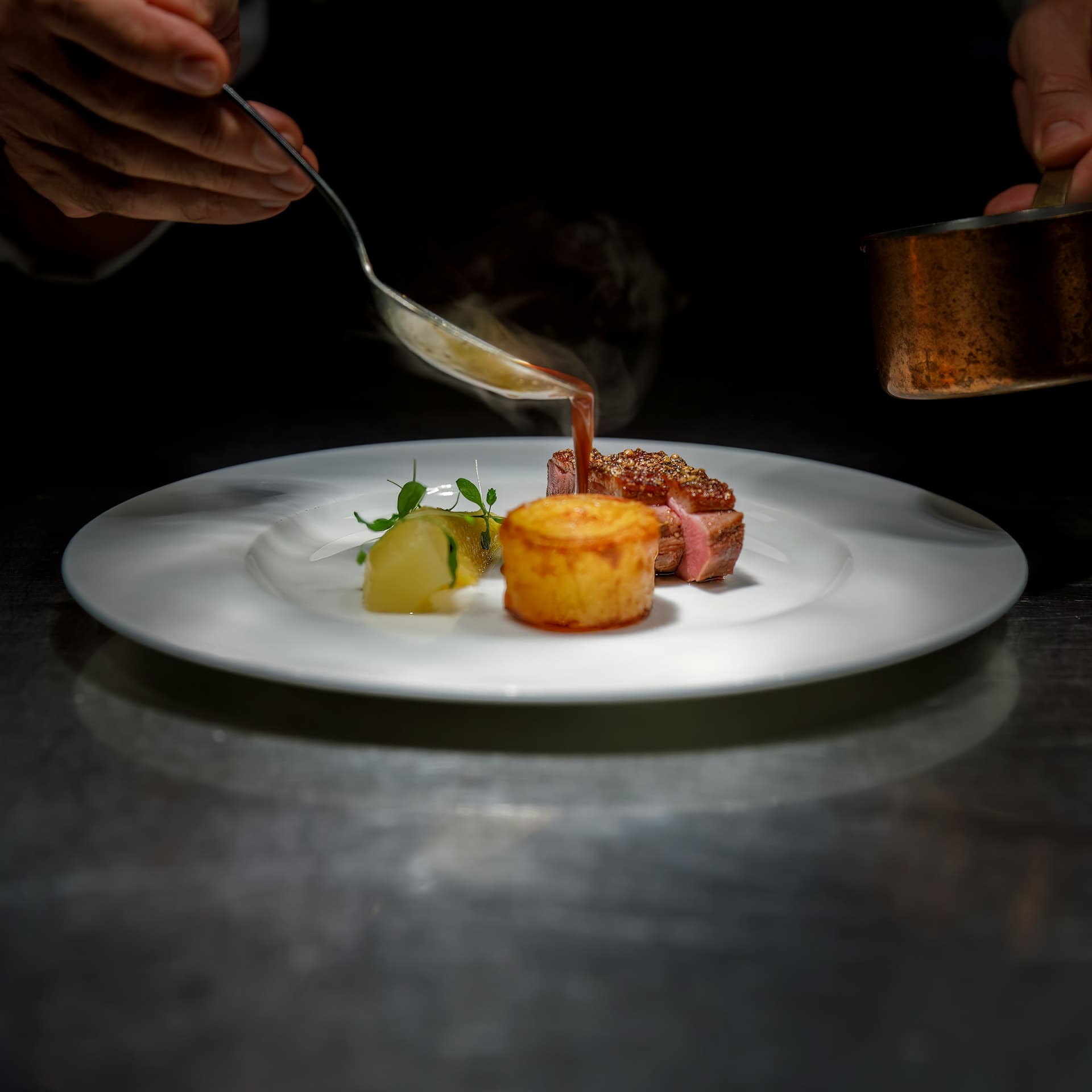 A sauce poured over a plated dish in a dark kitchen