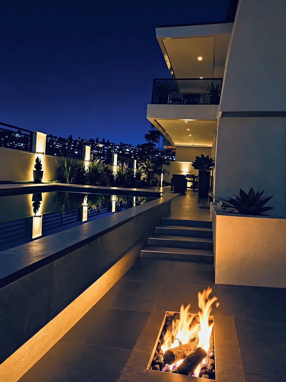 A fire pit and the pool terrace at night, with the city lights beyond. Amahoro, Kibagabaga.