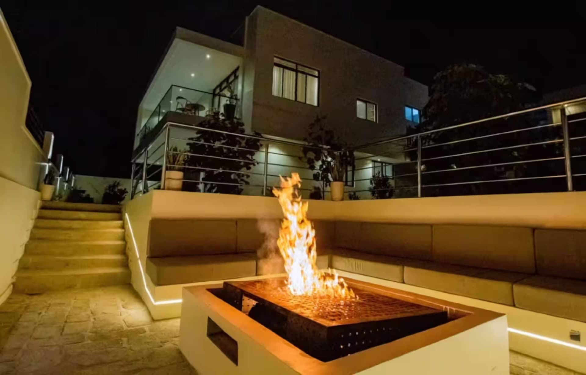 A fire pit burning in the sunken lounge at night, with the villa above. Amahoro, Kibagabaga.