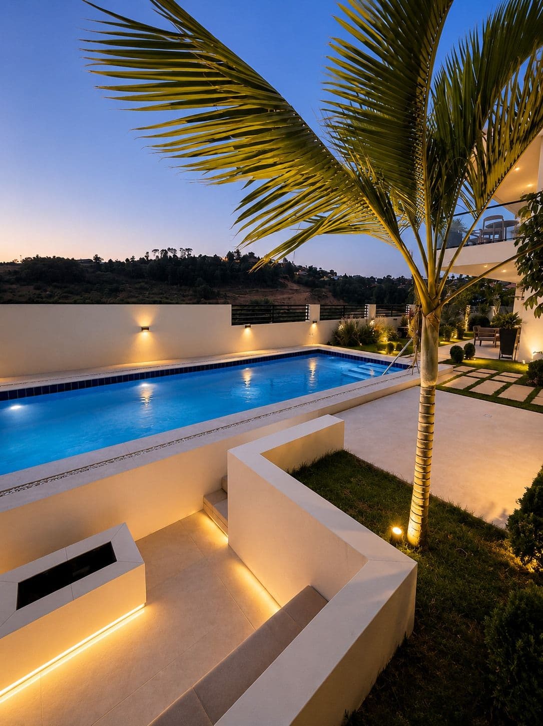 A tall palm and the pool, with lit steps at dusk. Amahoro, Kibagabaga.
