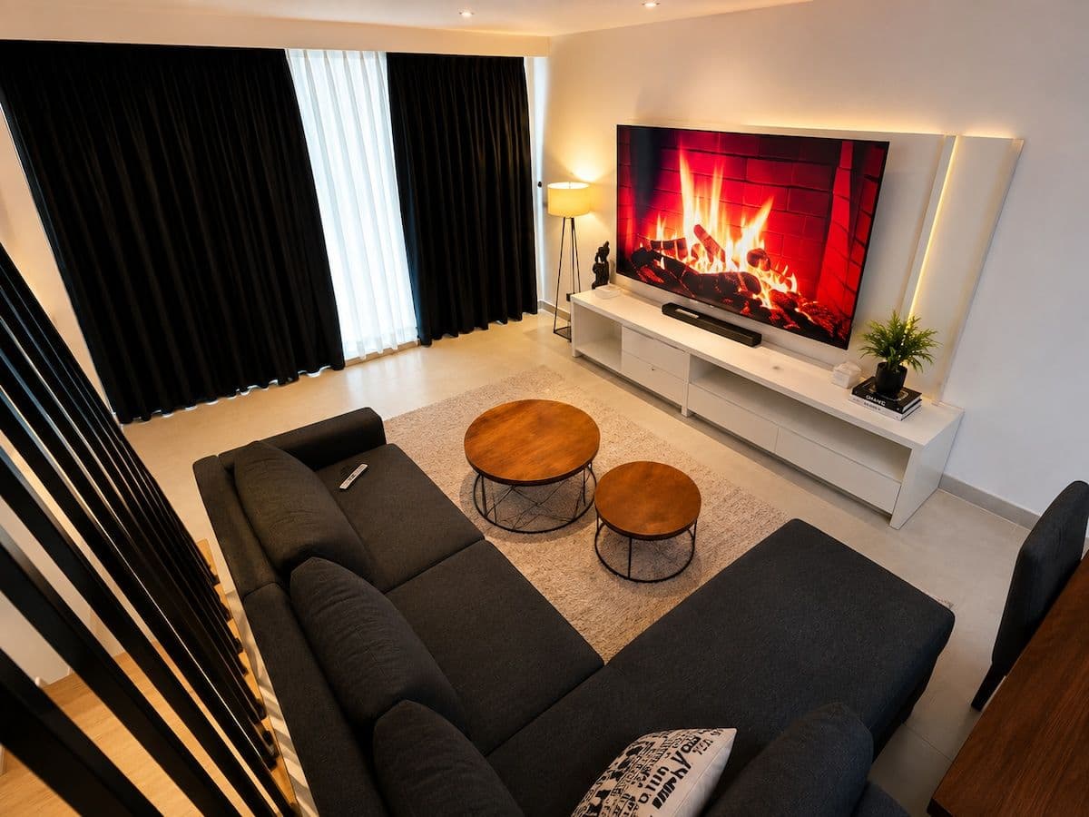 The living room from above, with a sectional sofa facing a wall TV glowing like a fireplace. Ikaze.