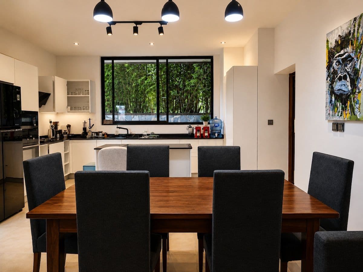 The wooden dining table at Ikaze, with the kitchen and a window onto bamboo, Niboye, Kigali