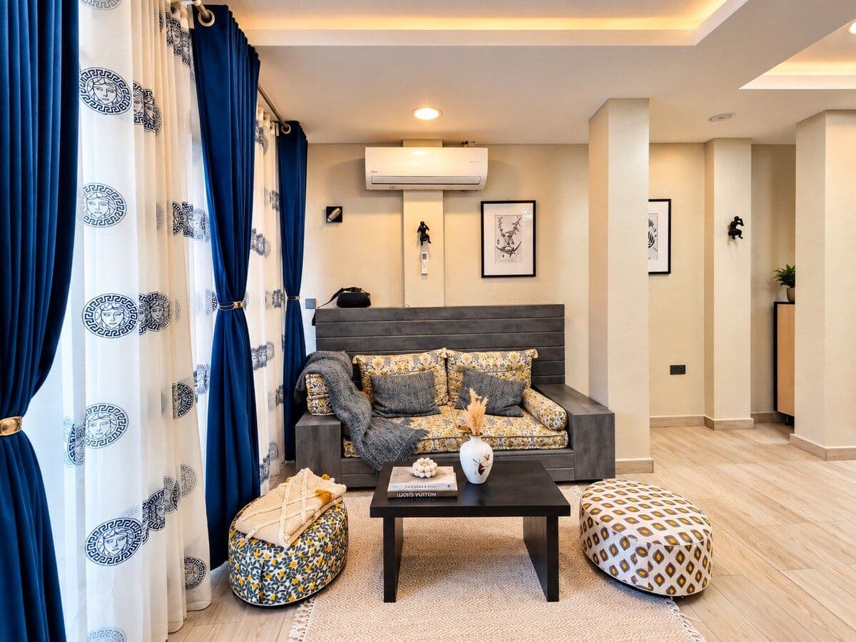 A sitting nook, with a grey sofa and patterned floor poufs. Irebero, Rebero.