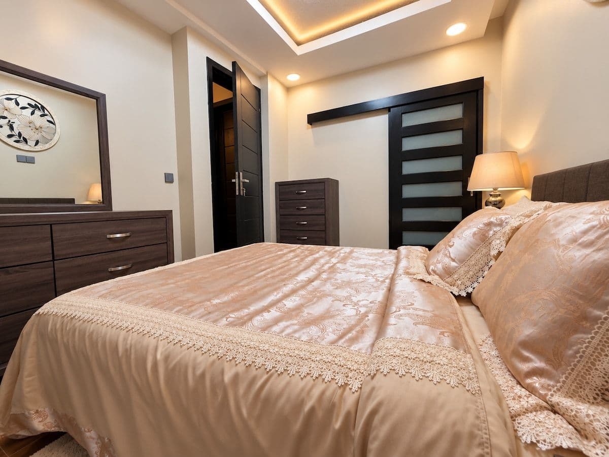 A bedroom with gold satin bedding and a warm bedside lamp. Irebero, Rebero.