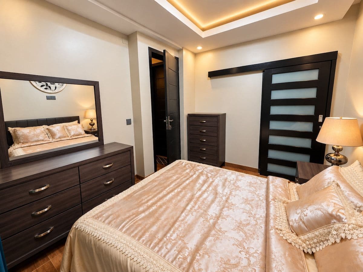 A bedroom in gold bedding, with a long mirror and a dresser. Irebero, Rebero.