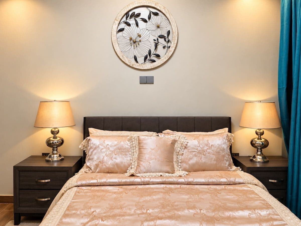 A bed beneath a round floral wall piece, between two brass lamps. Irebero, Rebero.