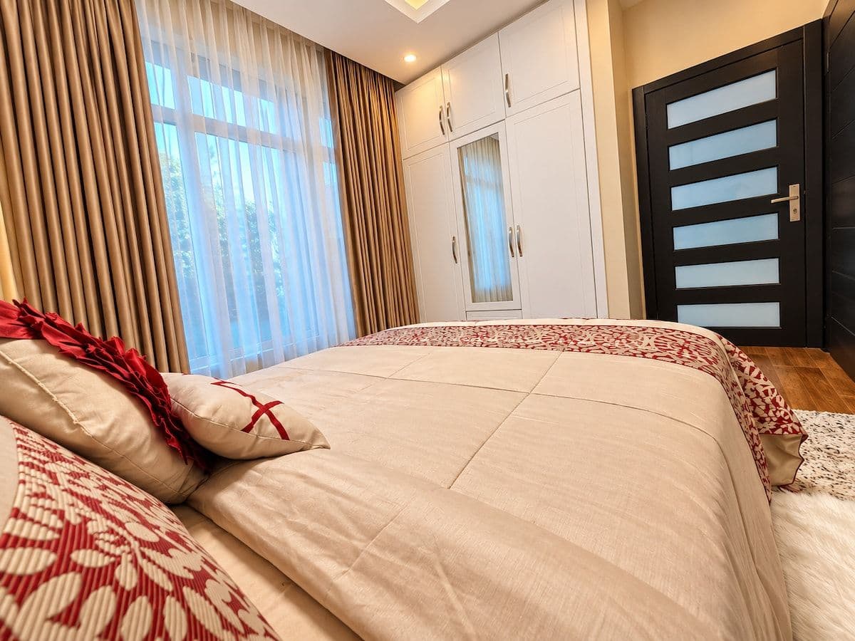 A bed with red-patterned pillows beside a tall window. Irebero, Rebero.