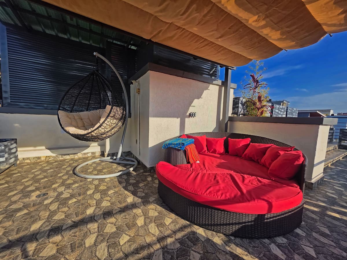 The rooftop lounge, with a red daybed, a hanging chair and a canopy, in sunshine. Irebero, Rebero.