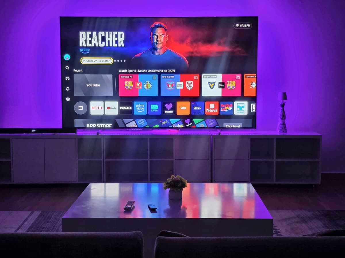 The cinema lounge in violet light, with the 100-inch screen above a long low cabinet. Urugwiro, Kacyiru.